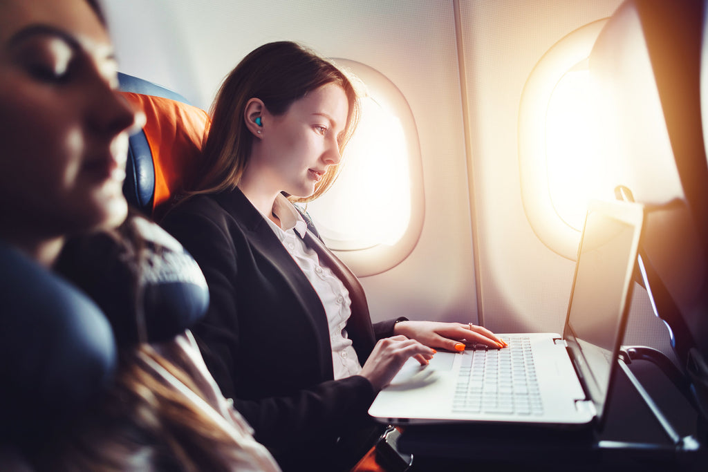 Woman on plane, using laptop, with foam earplug in her ear